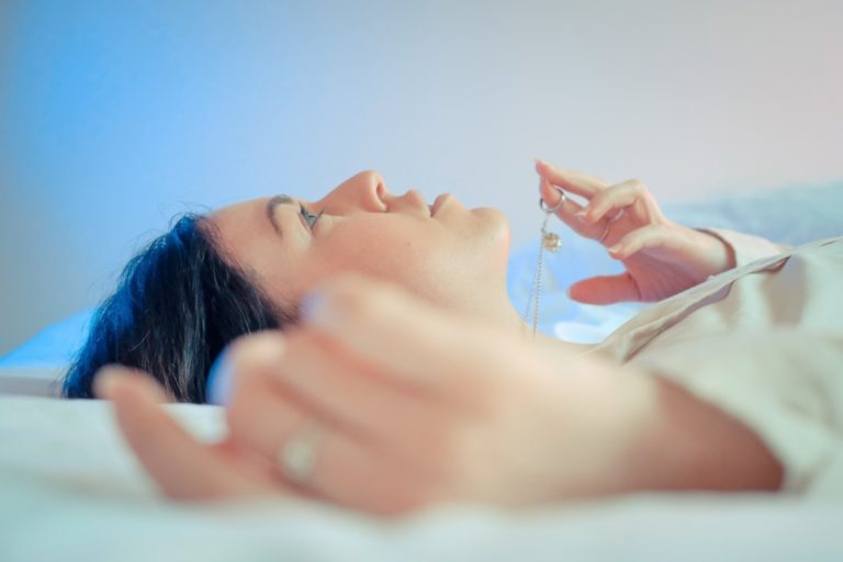 women lying down pensive, playing with one necklace in her fingers looking at the ceiling