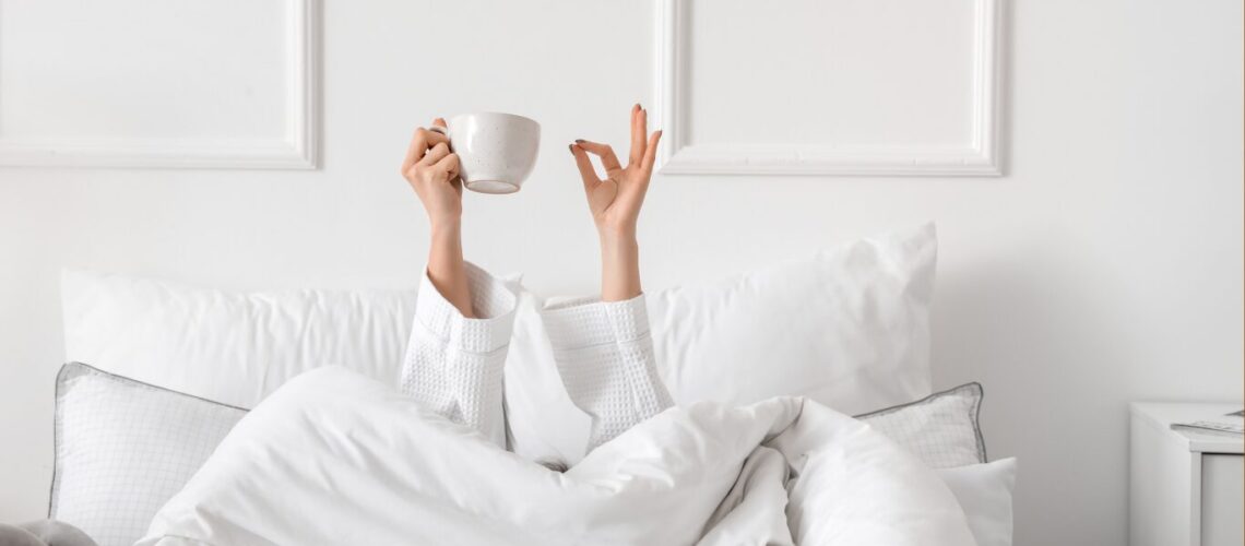 woman in a white bed, can only see arms raised, making the sign that she is fine and holding a cup